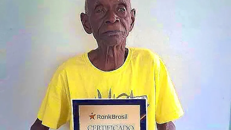 A photo of the Brazilian centenarian, the world's oldest human, with a warm smile and a twinkle in his eye, surrounded by family and friends, with a colourful background that reflects his vibrant personality and remarkable life story
