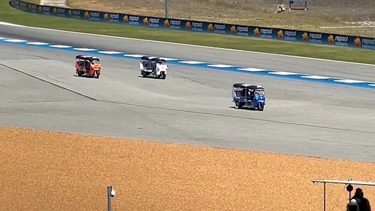 A tuk-tuk navigates the track during the MotoGP warm-up session in Thailand, surrounded by cheering fans and colourful scenery, with the primary keyword being MotoGP