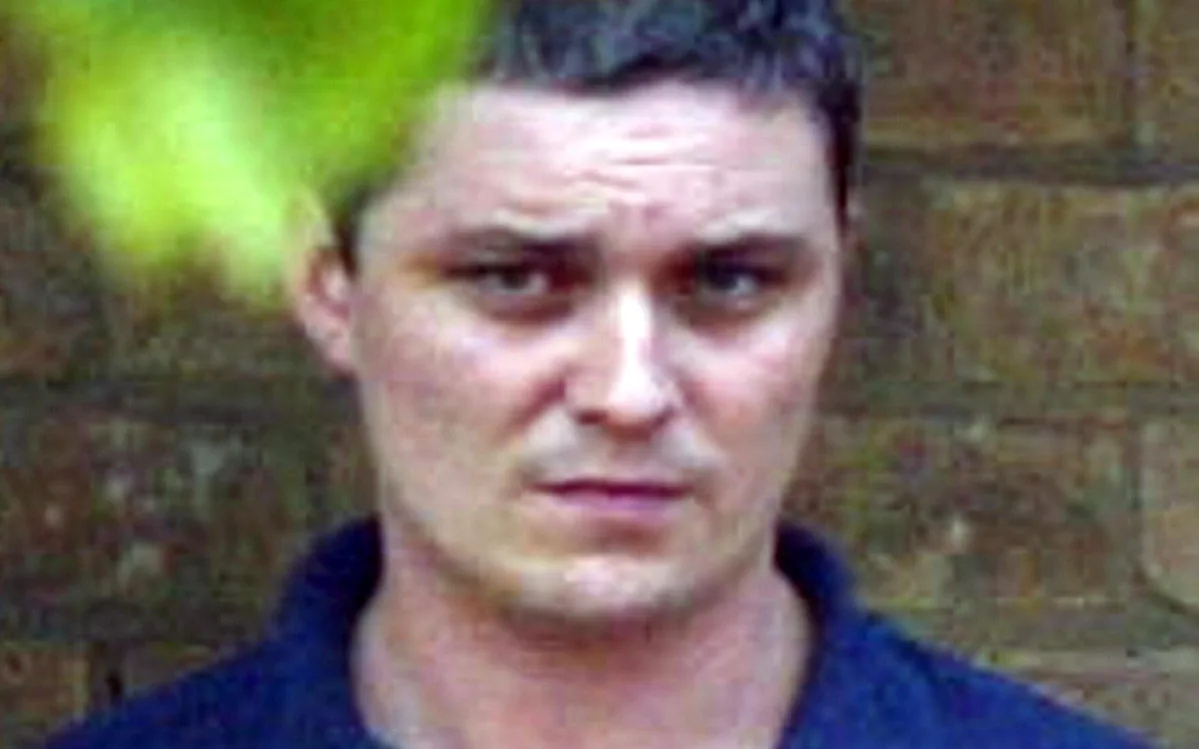 A sombre image of a prison cell, with a hint of darkness and despair, representing the tragic fate of Ian Huntley, a man whose life has been marred by violence and tragedy, and is now on life support after a brutal prison attack