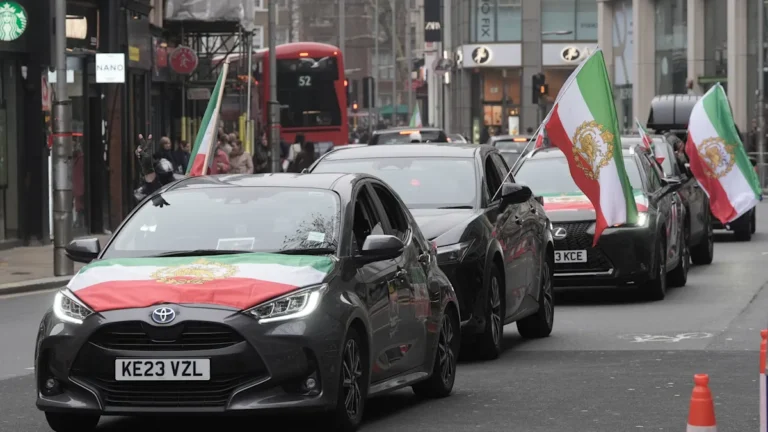 A crowd of demonstrators gather outside the Iranian embassy, holding placards and banners in support of peace and unity, with a strong message against war and conflict