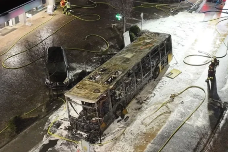 A bus engulfed in flames, with smoke billowing into the air, following a devastating fire in Switzerland that resulted in the loss of six lives, with the primary keyword being Swiss bus fire