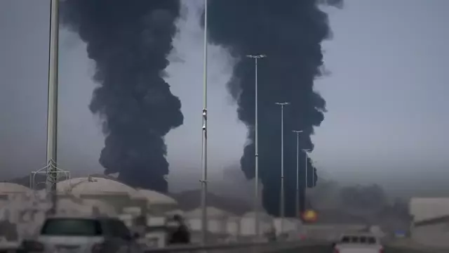 A photograph of an oil refinery in the Middle East, with a US flag and an Iranian flag in the foreground, symbolising the conflict between the two nations over oil-critical targets