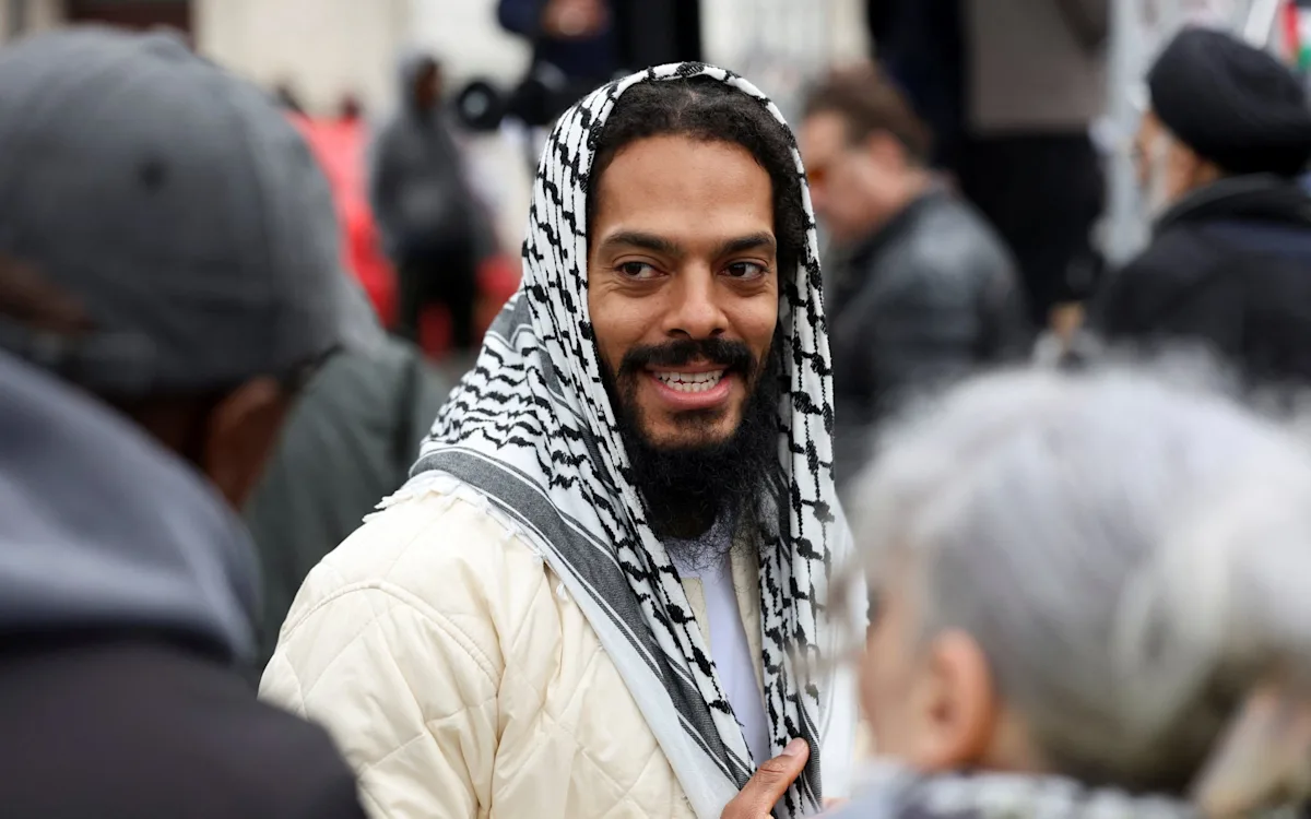 Bobby Vylan leading chants of 'death, death to the IDF' at a pro-Iran rally, sparking controversy and outrage, with a crowd of people in the background, some of whom are holding signs and banners in support of Iran, while others look on in shock and disgust, highlighting the divisive nature of the incident and the need for careful consideration and respectful behaviour