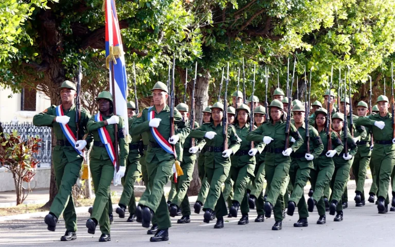 A Cuban soldier standing guard in front of the Cuban flag, with a backdrop of the Havana skyline, as the country prepares for potential US military action and rising tensions