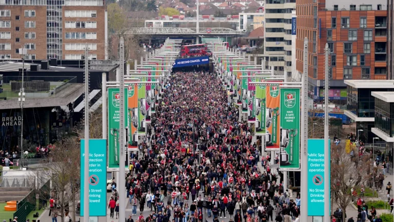 Police officers standing outside a football stadium, with a crowd of fans in the background, highlighting the importance of stadium safety and security, particularly in relation to tailgating behaviour
