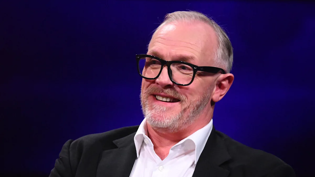 Greg Davies, comedian and host of Taskmaster, to host Bafta TV awards 2026, posing with a Bafta award, with a colourful background, showcasing his unique behaviour and style, as a popular figure in British television