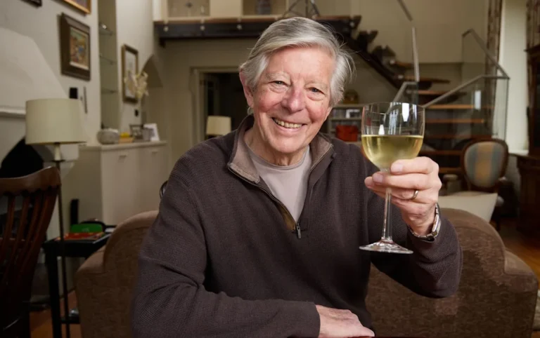 An 80-year-old woman laughing and chatting with friends at a social gathering, surrounded by a vibrant colour scheme and lively atmosphere, highlighting the importance of social behaviour and staying connected in later life