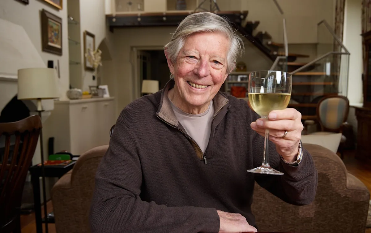 An 80-year-old woman laughing and chatting with friends at a social gathering, surrounded by a vibrant colour scheme and lively atmosphere, highlighting the importance of social behaviour and staying connected in later life