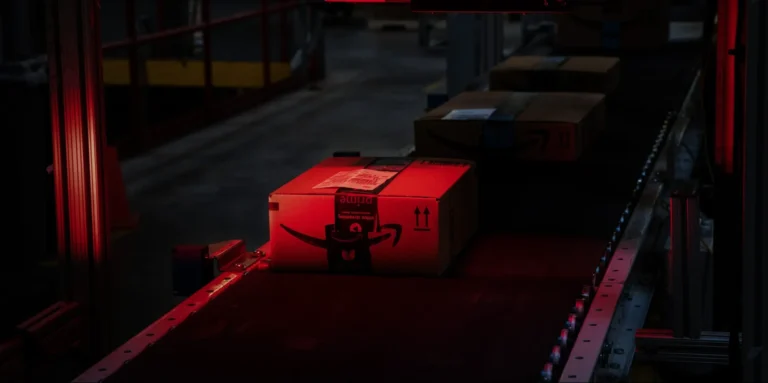 A photo of a person holding a PC component, with a surprised expression, surrounded by multiple boxes of components, highlighting the issue of Amazon's packaging errors and the impact on UK retailers