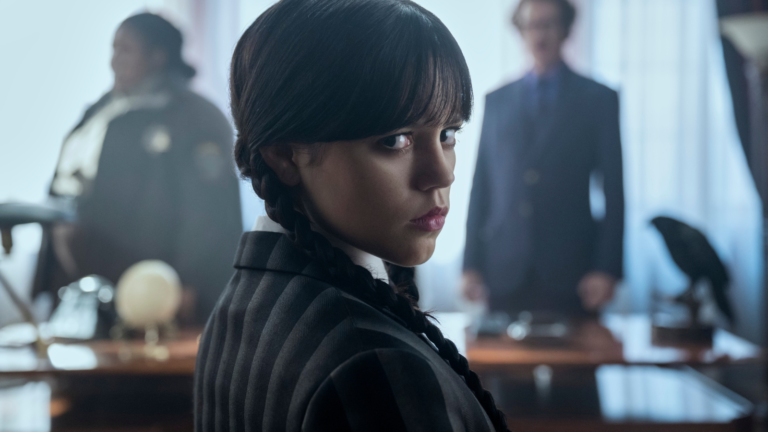 Wednesday Addams, played by Jenna Ortega, stands in front of a spooky mansion, with a full moon shining in the background. The image is dark and atmospheric, with a hint of supernatural mystery. The show's logo is emblazoned on the top, with the tagline 'New season, new terror' written below.