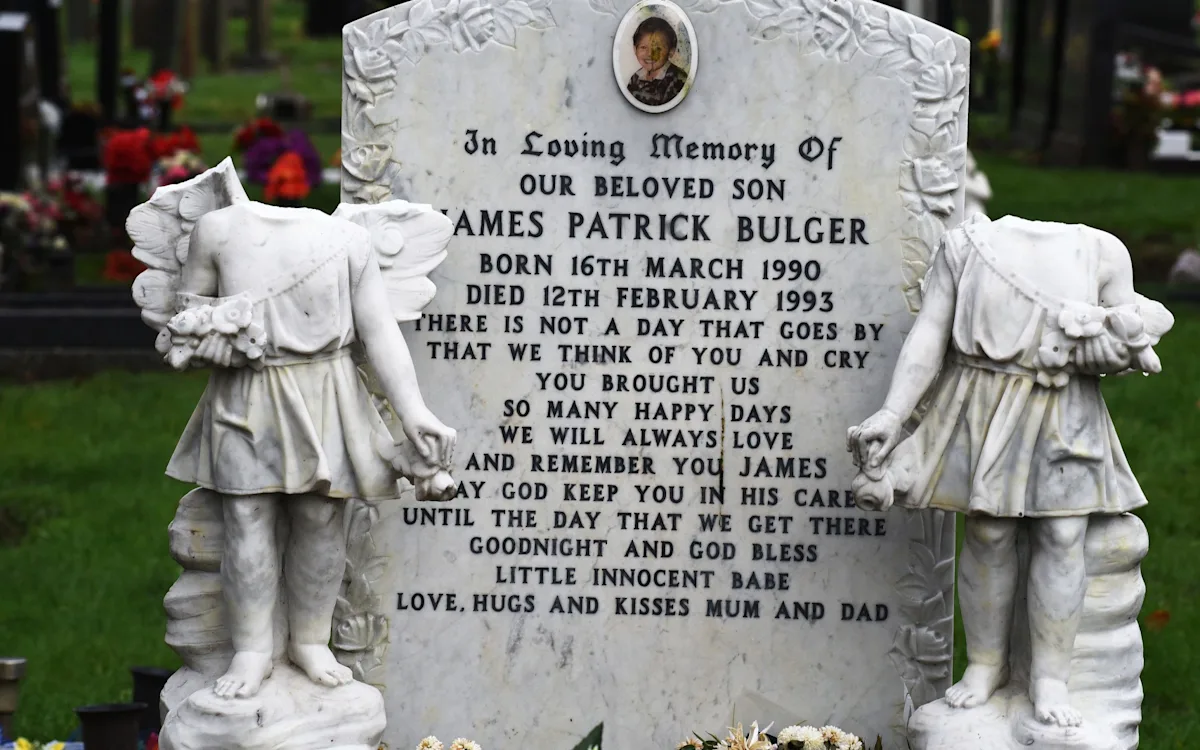 A photo of James Bulger's grave, with flowers and tributes left in his memory, highlighting the senseless vandalism that has sparked widespread outrage and condemnation, with a primary focus on the James Bulger grave vandalism incident