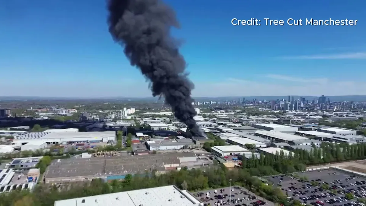 Aerial view of the Trafford Park fire, with flames and smoke billowing from the affected buildings, highlighting the severity of the incident and the importance of fire safety measures