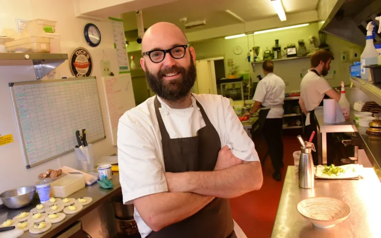 A bottle of red wine being poured into a glass, with a blurred background of a busy restaurant, highlighting the primary keyword of house wine and the changing behaviour of consumers in the food industry
