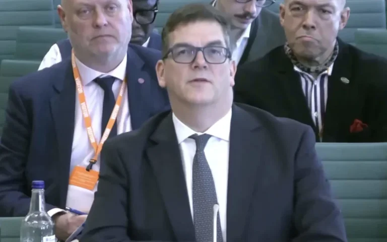 A man wearing a cravat and a suit, blending in with government officials at a high-profile event, with a mix of curiosity and suspicion surrounding his presence, as people try to uncover the mystery of the cravat-wearing gatecrasher