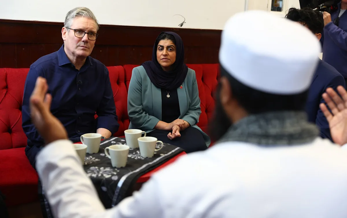 A group of Muslim voters discussing their political allegiance, with a Labour Party poster in the background, highlighting the party's struggle to retain their support due to its handling of Islamophobia