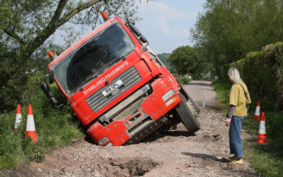 A massive pothole swallows a pothole repair truck, highlighting the challenges faced by road maintenance crews in their daily work to fix potholes and ensure road safety, with the primary keyword being pothole repair