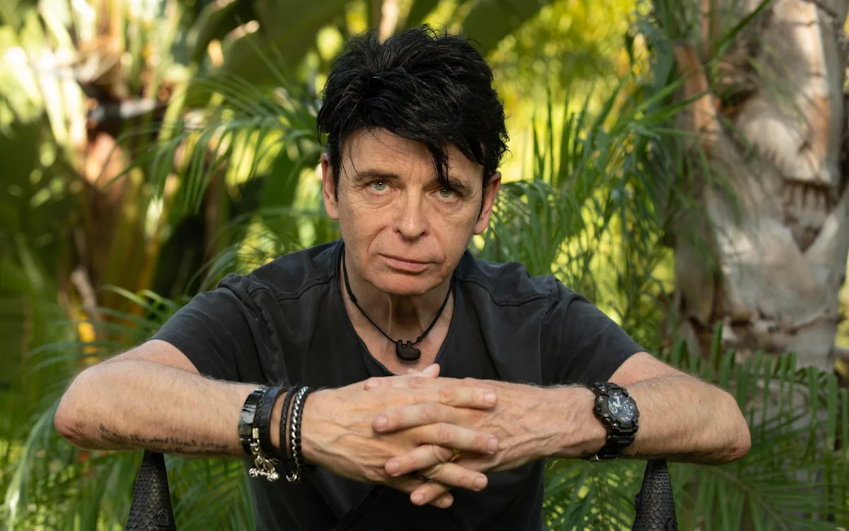 Gary Numan performing on stage, surrounded by a colourful array of synthesizers and guitars, his music a testament to his innovative spirit and creative genius, with a focus on his primary keyword, synth-pop