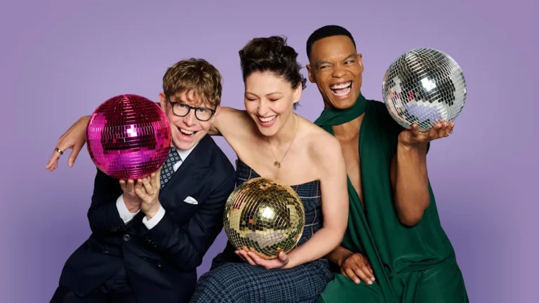 The new hosts of Strictly Come Dancing, Emma Willis, Josh Widdicombe, and Johannes Radebe, pose together in a promotional photo, surrounded by glittering dance costumes and a colourful background, with a focus on the popular dance competition