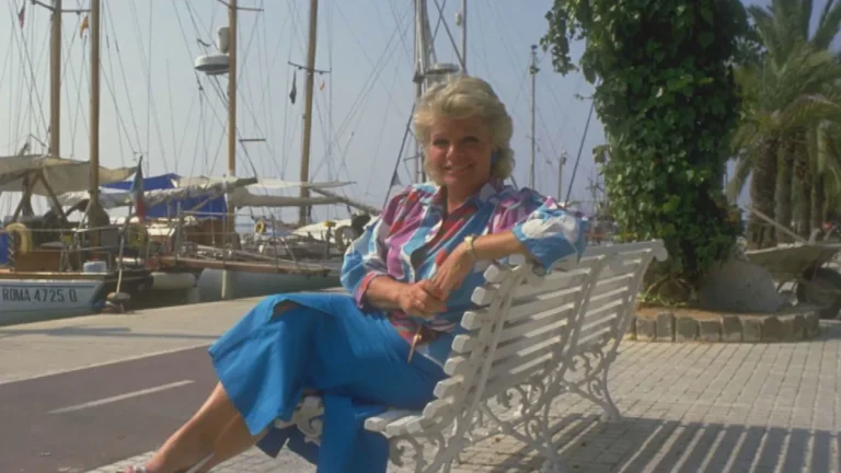 Judith Chalmers, renowned TV presenter and host of Wish You Were Here, smiling and standing in front of a picturesque landscape, embodying her love for travel and exploration