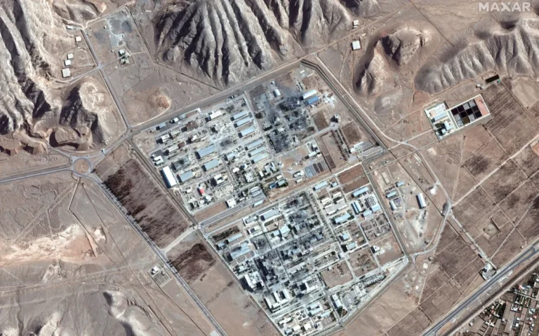 Iranian nuclear facility with a sign reading 'uranium enrichment' in the foreground, with a ship passing through the Hormuz Strait in the background, symbolising the country's decision to surrender its uranium and open the strategic waterway