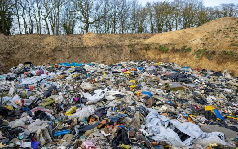 A pile of rubbish and waste dumped in a field, with a sign in the background reading 'No Fly-Tipping', highlighting the issue of illegal dumping in the UK, with Tory councils being criticised for their handling of the problem