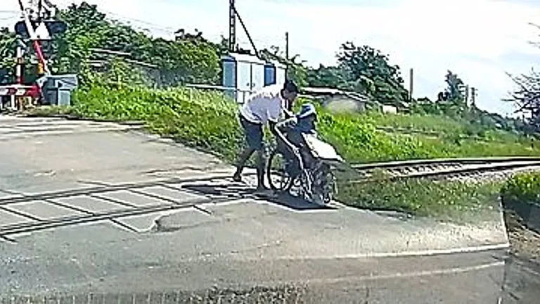 A wheelchair vendor is rescued by a heroic driver at a railway crossing, with a train approaching in the background, highlighting the importance of safety measures and accessibility for people with disabilities