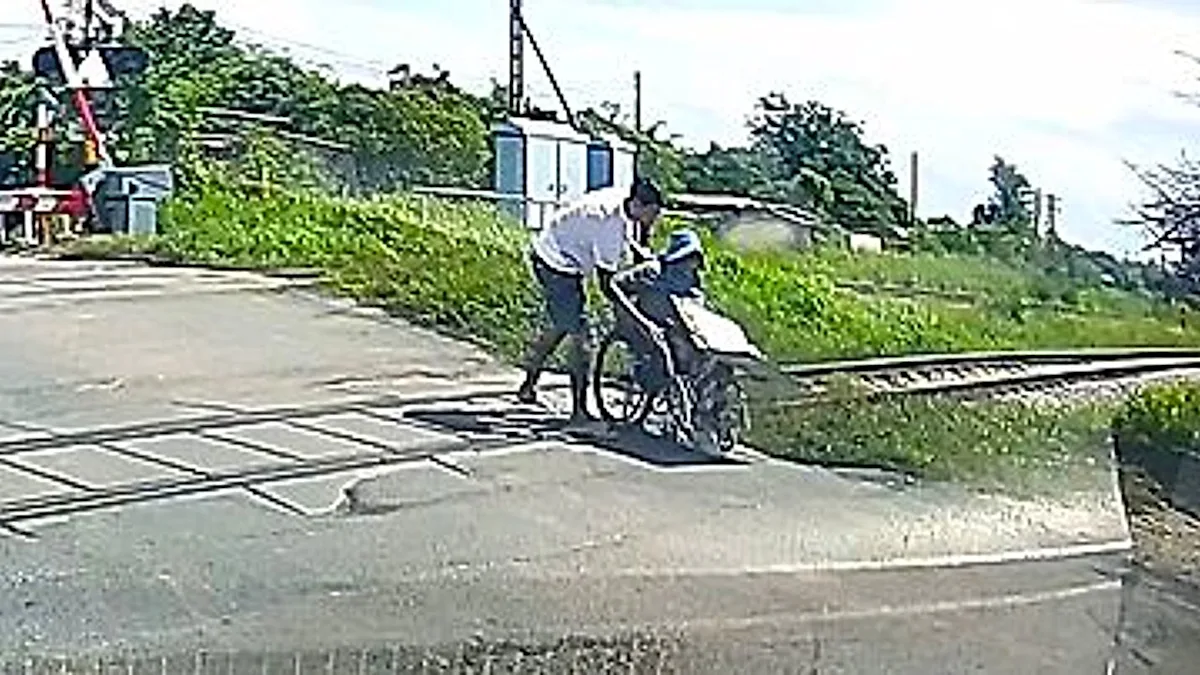A wheelchair vendor is rescued by a heroic driver at a railway crossing, with a train approaching in the background, highlighting the importance of safety measures and accessibility for people with disabilities