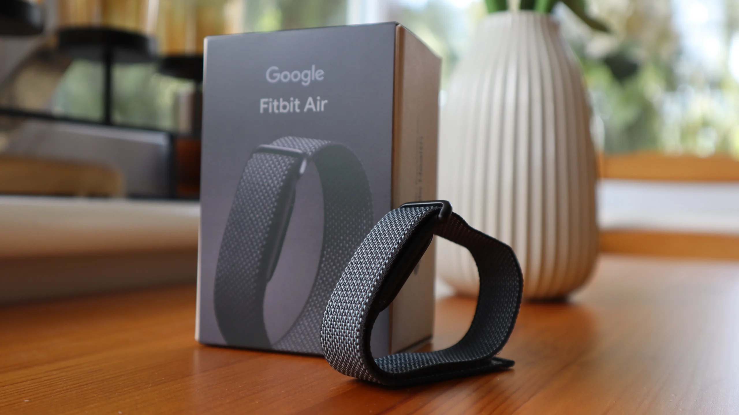 The Fitbit Air, a screenless fitness tracker with a discreet design, available in three colours: Obsidian, Lavender, and Berry. The device is shown on a person's wrist, with a fitness tracking app open on a smartphone in the background. The image showcases the device's minimalist design and focus on distraction-free tech, making it a must-have for fitness enthusiasts in the UK