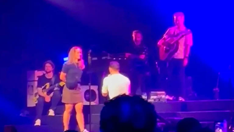 A man proposing to his partner on stage in front of a large crowd, with a shocked expression on his face as she rejects him, surrounded by a sea of stunned onlookers, highlighting the risks and complexities of public proposals and the importance of considering one's partner's feelings and boundaries