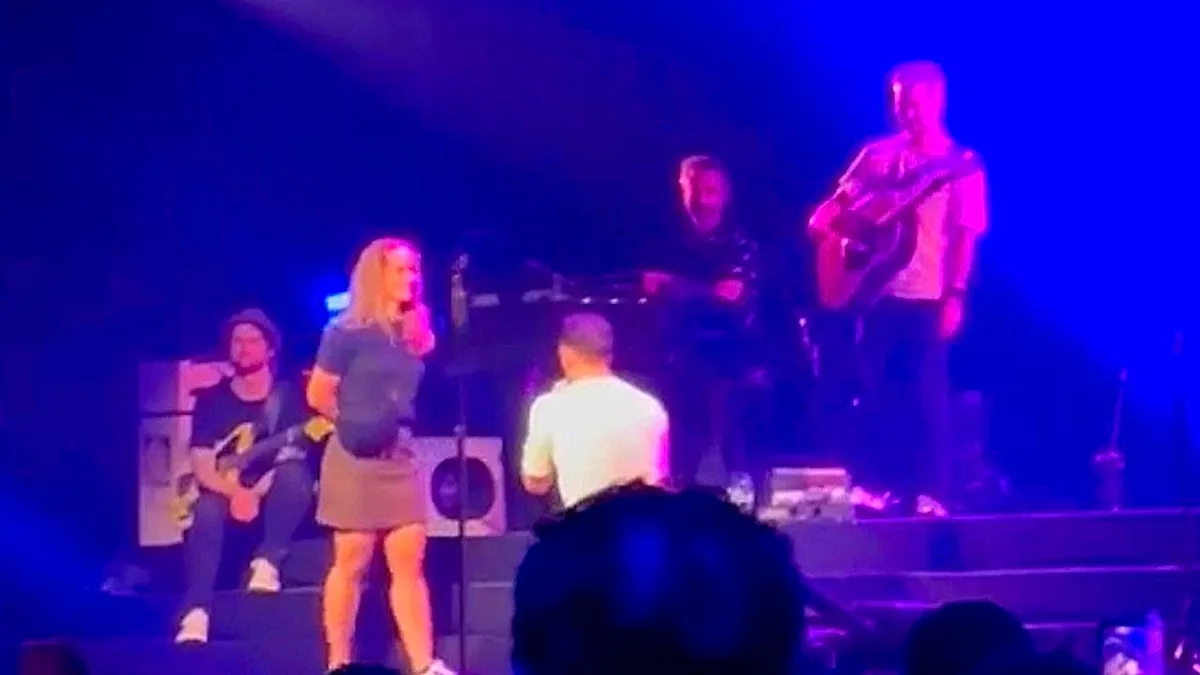 A man proposing to his partner on stage in front of a large crowd, with a shocked expression on his face as she rejects him, surrounded by a sea of stunned onlookers, highlighting the risks and complexities of public proposals and the importance of considering one's partner's feelings and boundaries