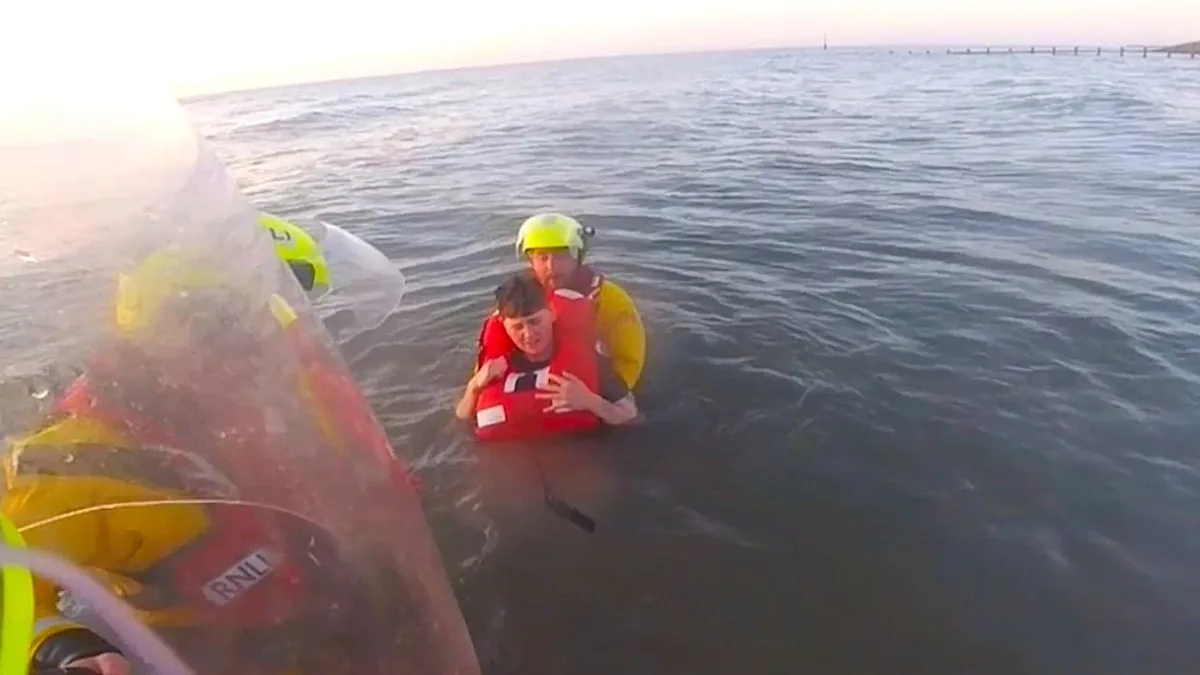 A dramatic photo of RNLI rescuers pulling a woman to safety from quicksand off the Welsh coast, with the tide closing in and the sun setting in the background, illustrating the dangers of quicksand and the bravery of the RNLI