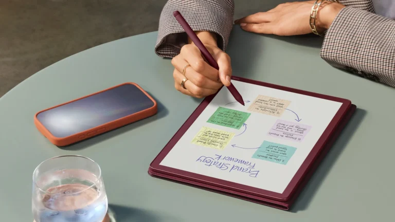 A person holding a Kindle Scribe eReader, with a colourful background and a book open on the device, showcasing the AI-powered features and note-taking capabilities of the latest Kindle Scribe range in the UK