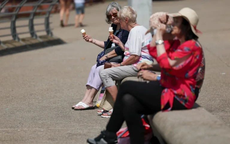 A descriptive image of a sunny day in the UK, with people enjoying the warm weather in a park, with a temperature gauge in the foreground showing high temperatures, highlighting the UK heatwave