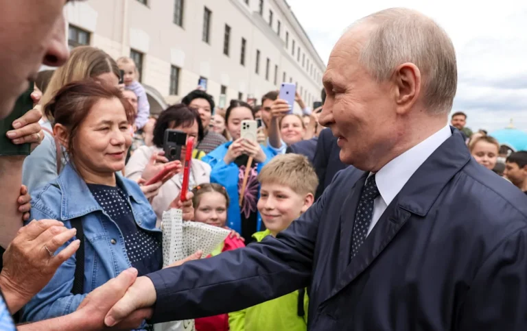 A crowd of people gathered around Putin, with a bodyguard in the background, highlighting the use of extras to manipulate public opinion in Russian politics