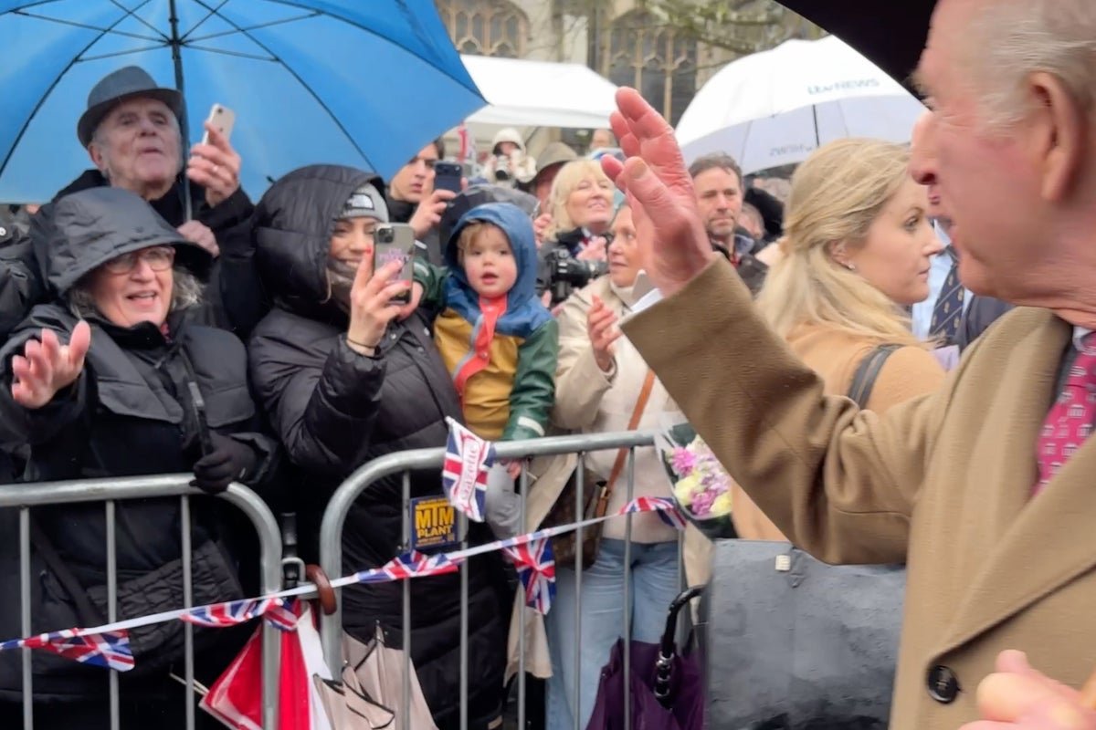 King Charles and Camilla, the Queen Consort, during a royal walkabout, surrounded by protesters holding signs referencing Prince Andrew's association with Jeffrey Epstein, highlighting the controversy and scrutiny surrounding the royal family