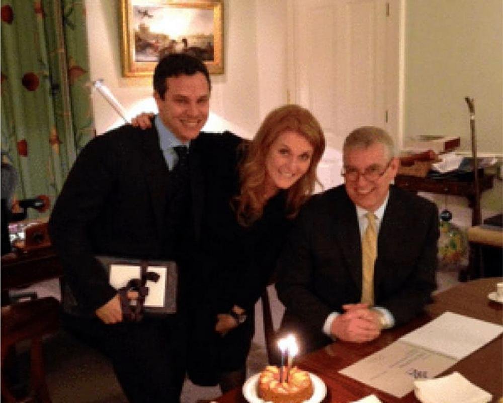A photo of Prince Andrew and Jeffrey Epstein together, with a descriptive caption about their controversial friendship and the colour of their behaviour, the image shows the two men smiling and shaking hands, with a backdrop of a luxurious setting, the image is a reminder of the scandal that has surrounded the royal family in recent years