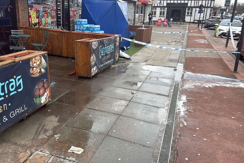 A Birmingham restaurant owner stands outside their establishment, looking concerned and fearful after a machete attack occurred in the area, highlighting the need for increased security measures and community support to prevent violent crime and ensure the safety of local businesses