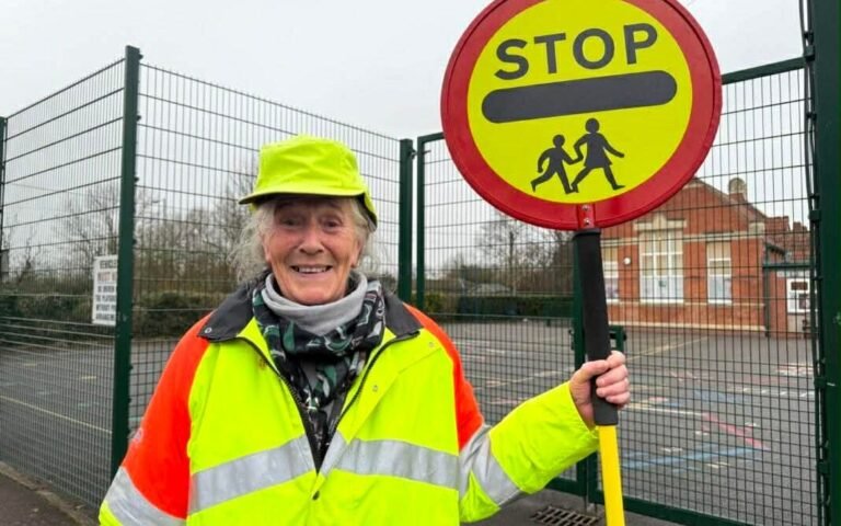 lollipop lady helping children cross road