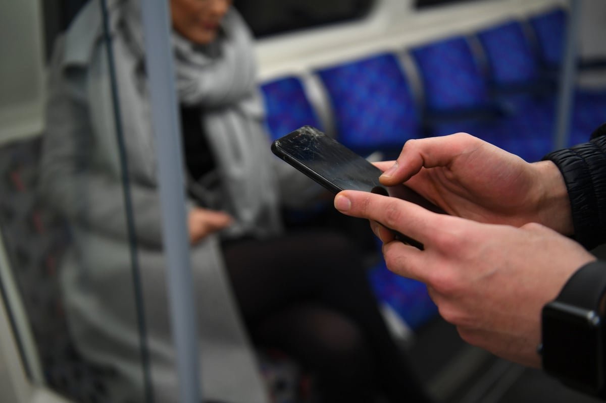 A person holding a mobile phone, with a shocked expression, as they realise they have been targeted in the London Tube SMS blaster scam, with the city of London in the background, highlighting the primary keyword phrase 'London Tube Scam'