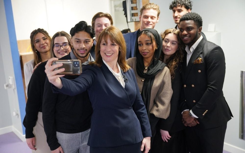 A group of young people in the UK, with a mix of emotions and reactions, as they consider the impact of Labour's youth minimum wage U-turn on their lives and futures, with a cityscape in the background, symbolising the urban environment and the economic reality of the UK's youth