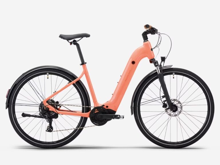 The Decathlon Rockrider E-ACTV 500 hybrid e-bike in Peach Orange, featuring a Yamaha motor and Suntour suspension, with a rider navigating through a bustling city street, showcasing the bike's versatility and comfort, with the primary keyword hybrid e-bike prominently featured