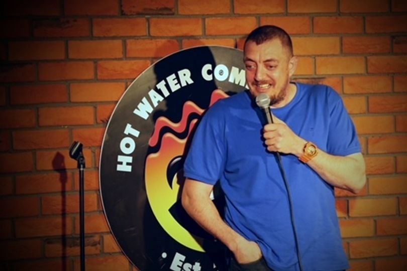 A photo of a Liverpool comedian on stage, with a microphone in hand, bringing laughter and joy to the audience with his unique brand of humour, comedy legend