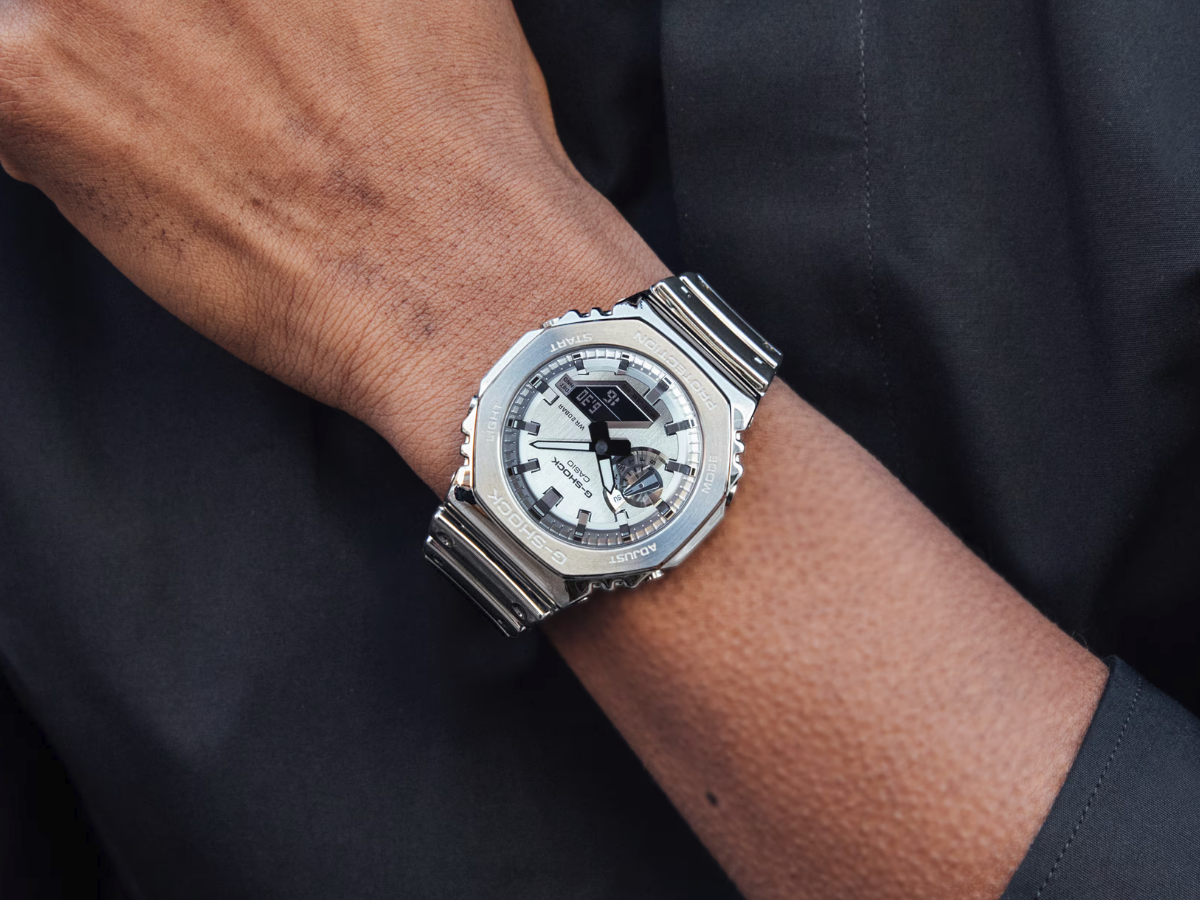 Casio G-Steel GM-2100YM series watch with metal bezel, featuring 200m water resistance and digital-analog functionality, available in silver and gold-tone variants