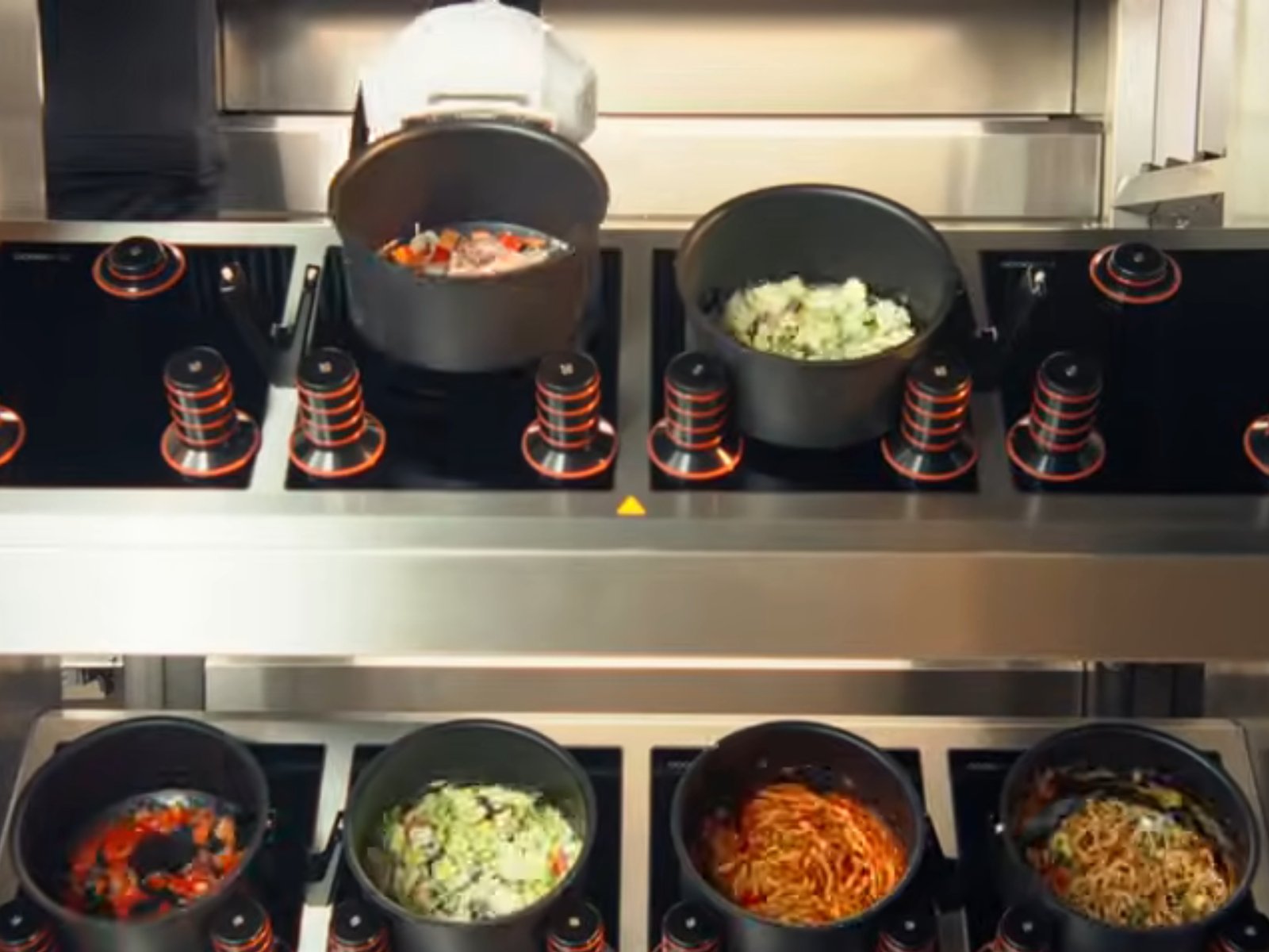 A futuristic kitchen with rows of cooking stations and a large screen displaying a menu, with the words 'Robot Kitchen' emblazoned on the side, showcasing the innovative technology that has won the Robotics Award 2026 in the UK, with the potential to prepare thousands of meals per day