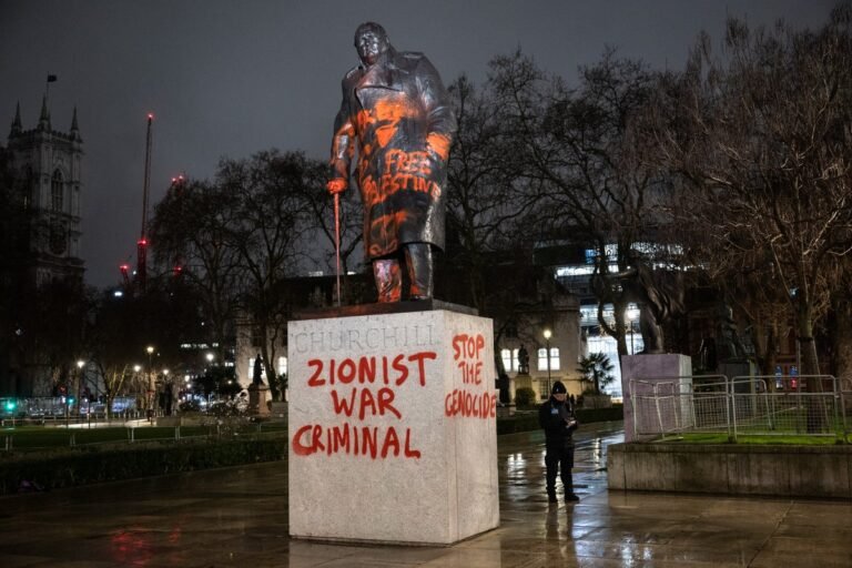 A photograph of the vandalised Churchill statue in London, featuring 'Zionist war criminal' graffiti, sparking outrage and debate about freedom of speech and preservation of historical monuments