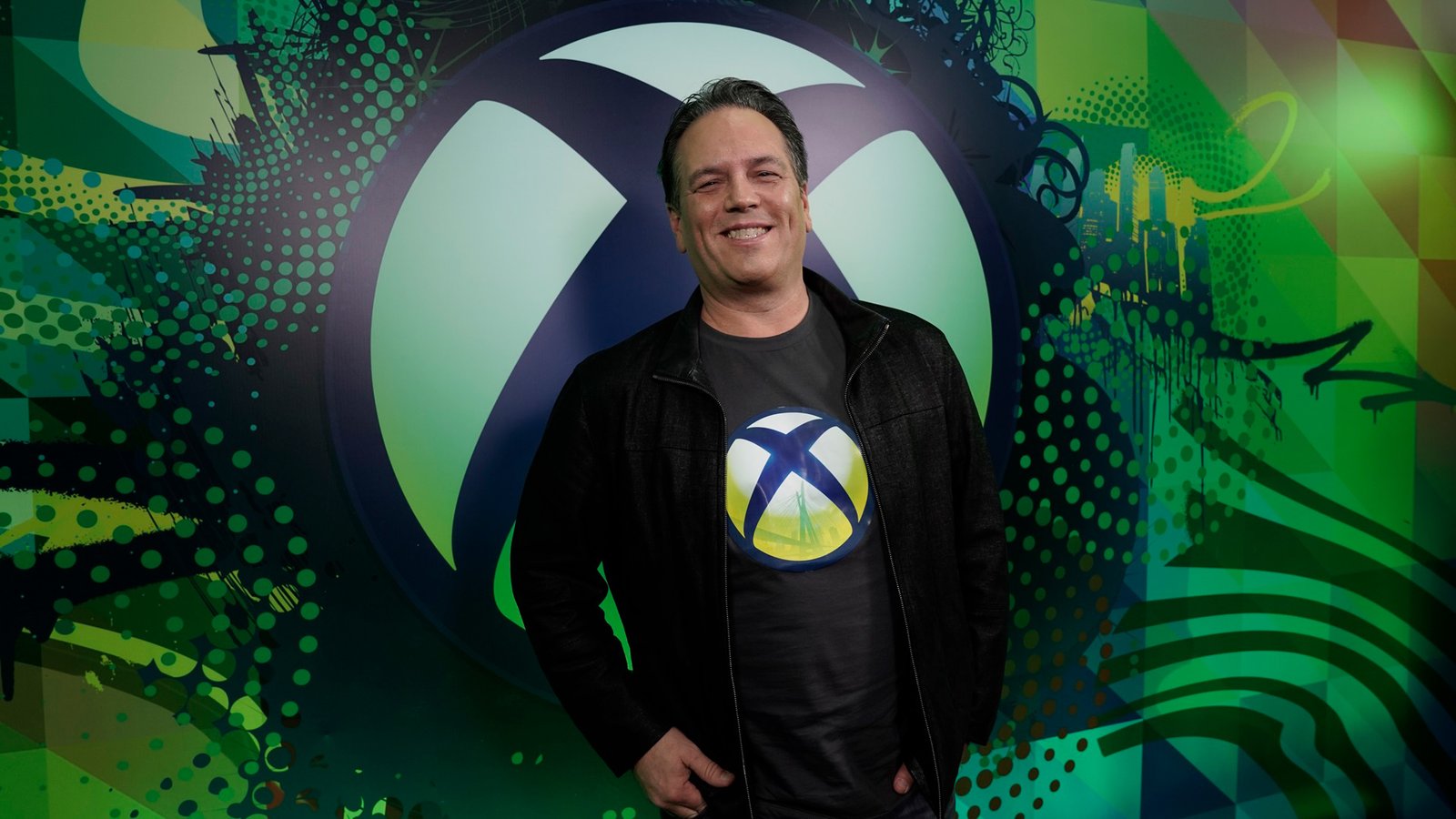 Phil Spencer, the former head of Xbox, is retiring after a 38-year career in the UK gaming industry. He is pictured here at a gaming event, surrounded by fans and colleagues. The image captures the colour and vibrancy of the UK gaming scene, which Spencer has been instrumental in shaping. His legacy will continue to inspire future generations of gamers and developers.