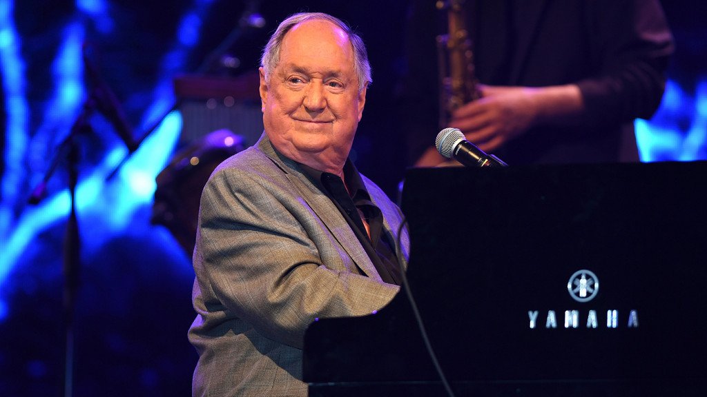 Neil Sedaka, a music legend with a career spanning over six decades, performing on stage with his iconic piano, leaving a lasting impact on the music industry with his unique voice and style