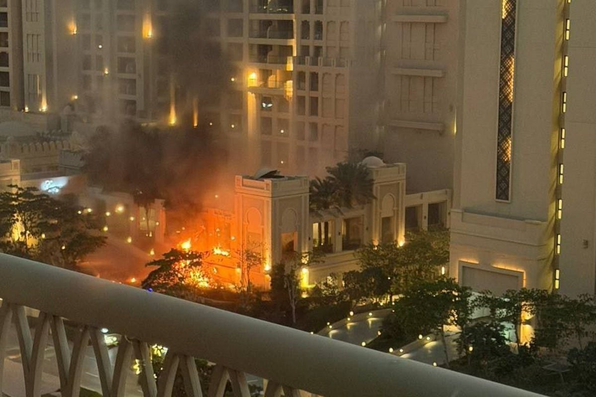 A massive fire engulfs the Fairmont Hotel in Palm Jumeirah, Dubai, during an air attack, with flames and smoke billowing into the air, as people watch in horror, with the primary keyword being Dubai hotel fire