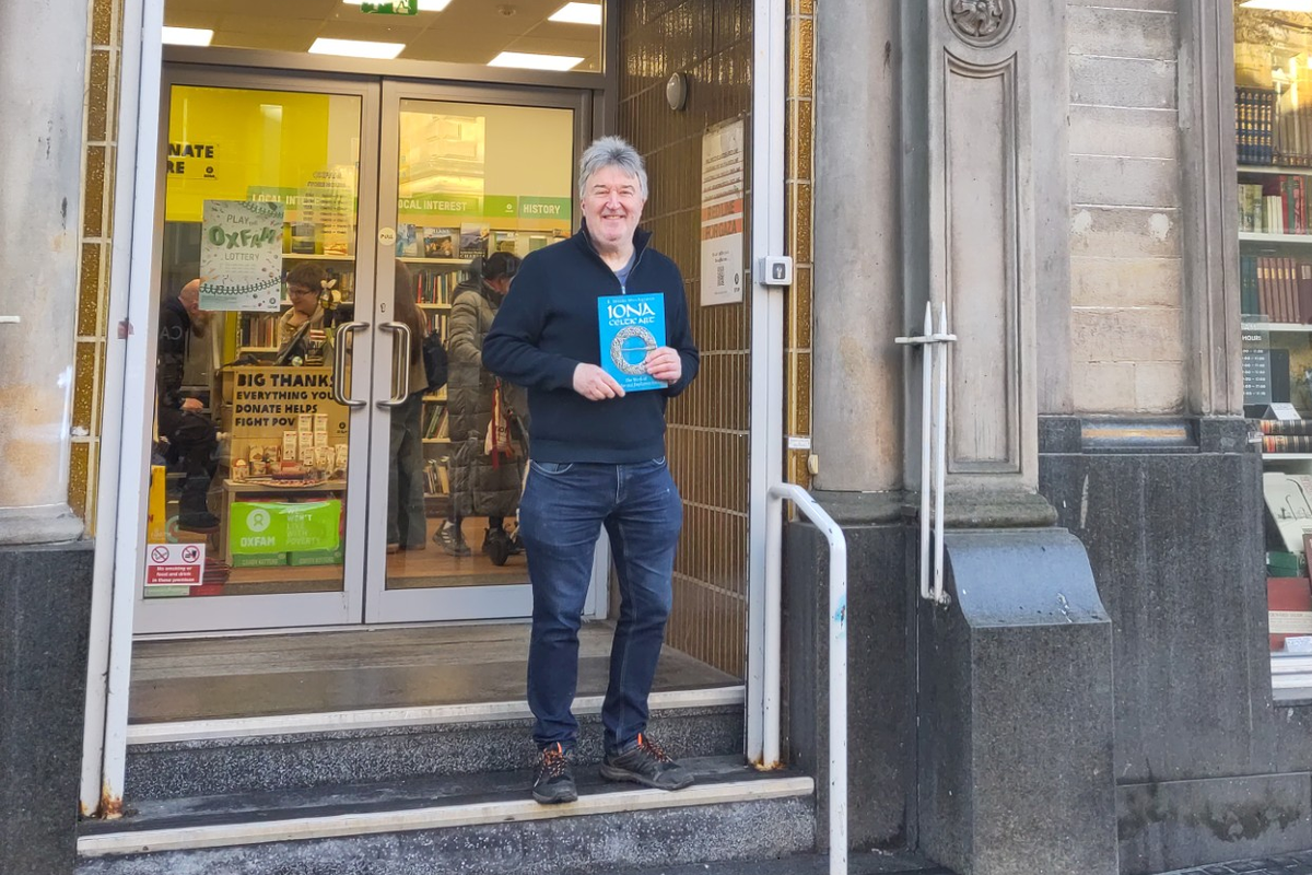A rare book collector holding a vintage book, with a look of excitement and joy on his face, surrounded by shelves of donated books in a charity shop, with the primary keyword 'rare books' featured prominently