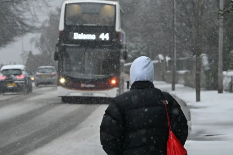 A snowy landscape in the UK, with a yellow weather warning sign in the foreground, indicating the Met Office's warning for snow and icy conditions, with a focus on winter weather and the UK's unpredictable climate.
